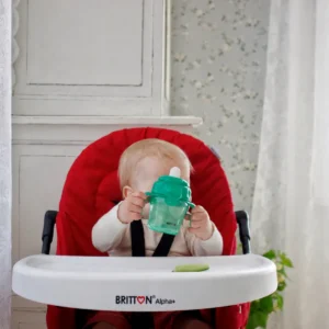 Baby holding the Britton green non-spill cup in a high chair