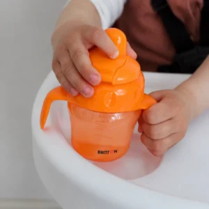 Child holding the Britton orange non-spill cup in a high chair
