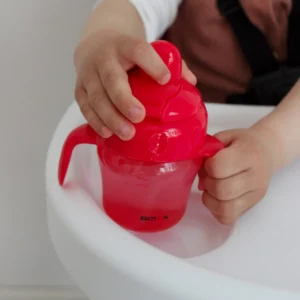 Child holding the Britton red non-spill cup in a high chair