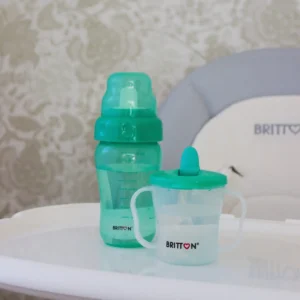 Britton First Cup 200 ml green with matching baby bottle on a high-chair tray