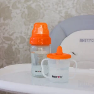 Britton First Cup 200 ml orange with matching baby bottle on a high-chair tray