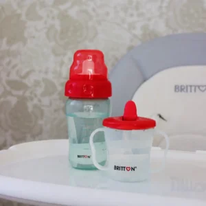 Britton First Cup 200 ml red with matching baby bottle on a high-chair tray